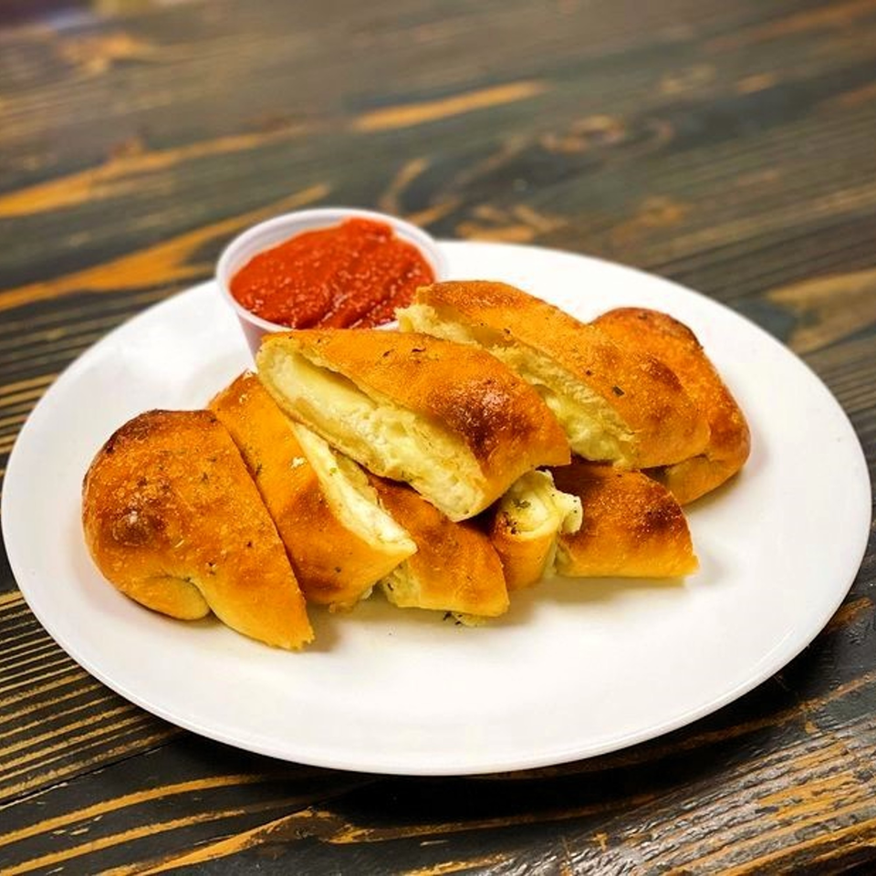 Golden-brown cheese breadsticks with herbs and a side of red marinara sauce on a white plate.