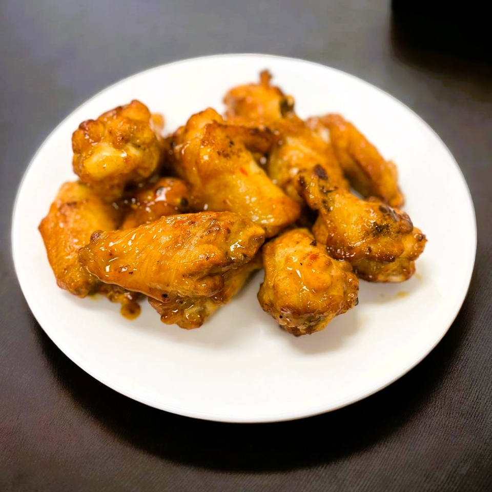 A white plate piled high with golden-brown, saucy chicken wings from Hatcher Pass Pizza.