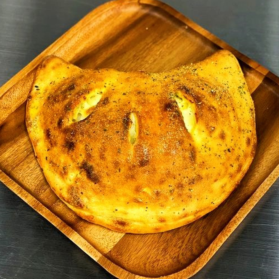 Golden-brown calzone with visible cheese filling, served on a square wooden tray.